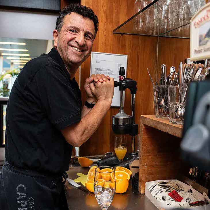 Glad medarbejder fra Café Cappuccino i Hvidovre skænker appelsin juice op. 